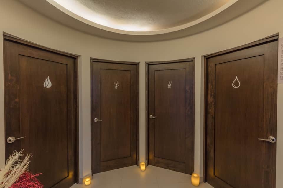Four dark wooden spa treatment room doors with elemental icons: flame, leaf, steam, and water droplet