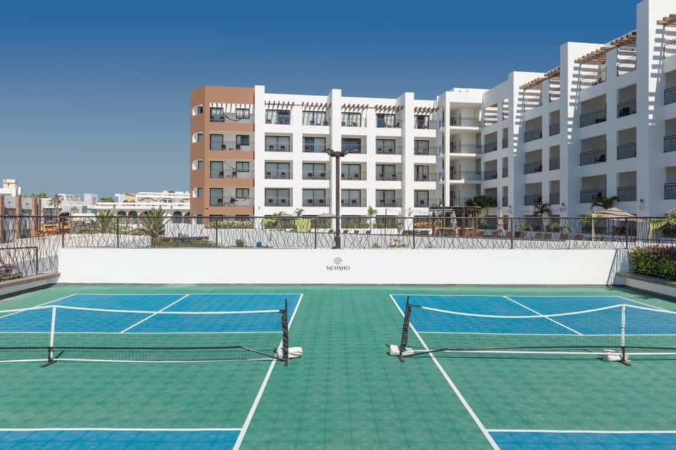 Tennis courts with blue and green surfaces at resort, white apartments in background