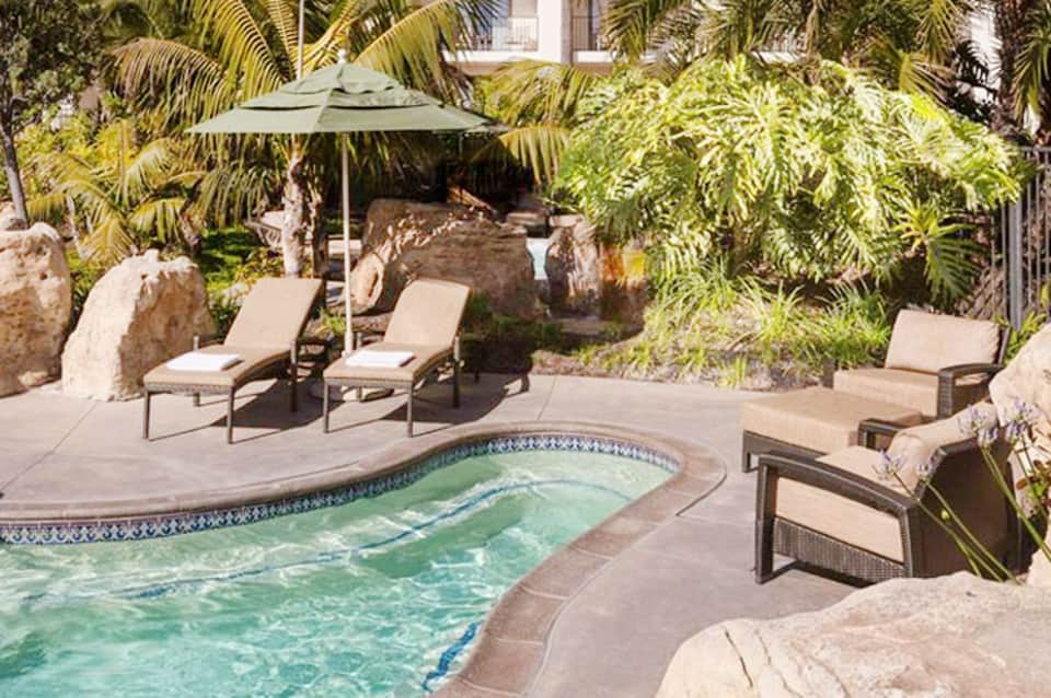 Luxury resort pool surrounded by lounge chairs, umbrella, and tropical plants with stone features
