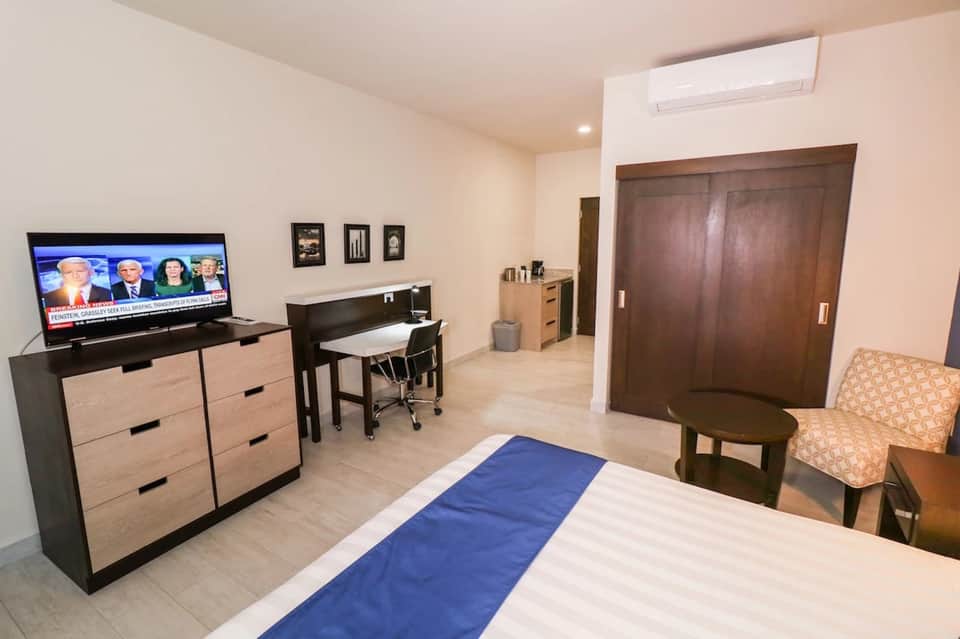Hotel room interior with bed, TV, work desk, dresser, and modern furnishings