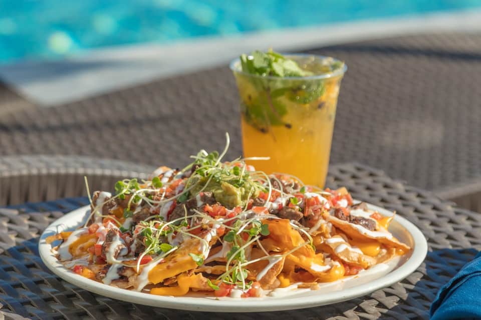 Pool-side appetizer plate with nachos and mojito cocktail on lounge chair table