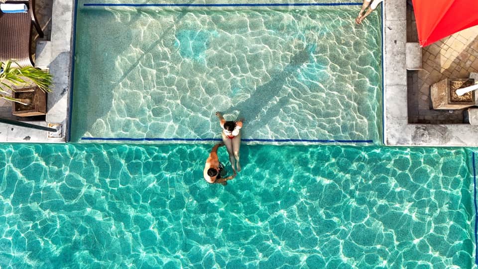 Overhead view of couple swimming in crystal-clear turquoise resort pool