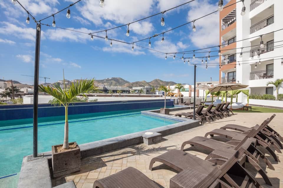 Rooftop pool with turquoise water, lounge chairs, string lights, and mountain views at a modern hotel resort