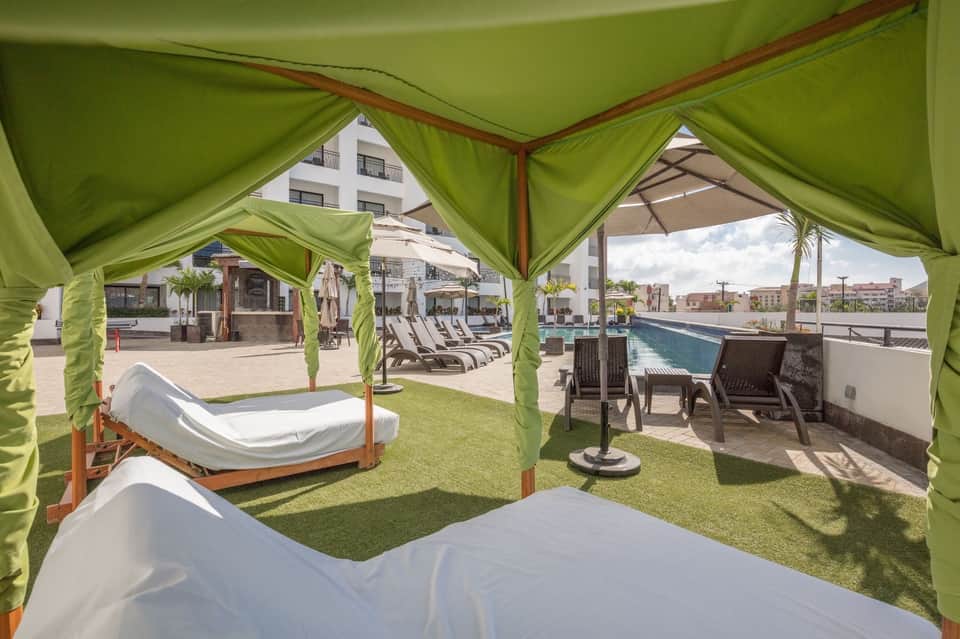 Luxury poolside cabanas with green curtains, white daybeds, and lounge seating overlooking the pool area