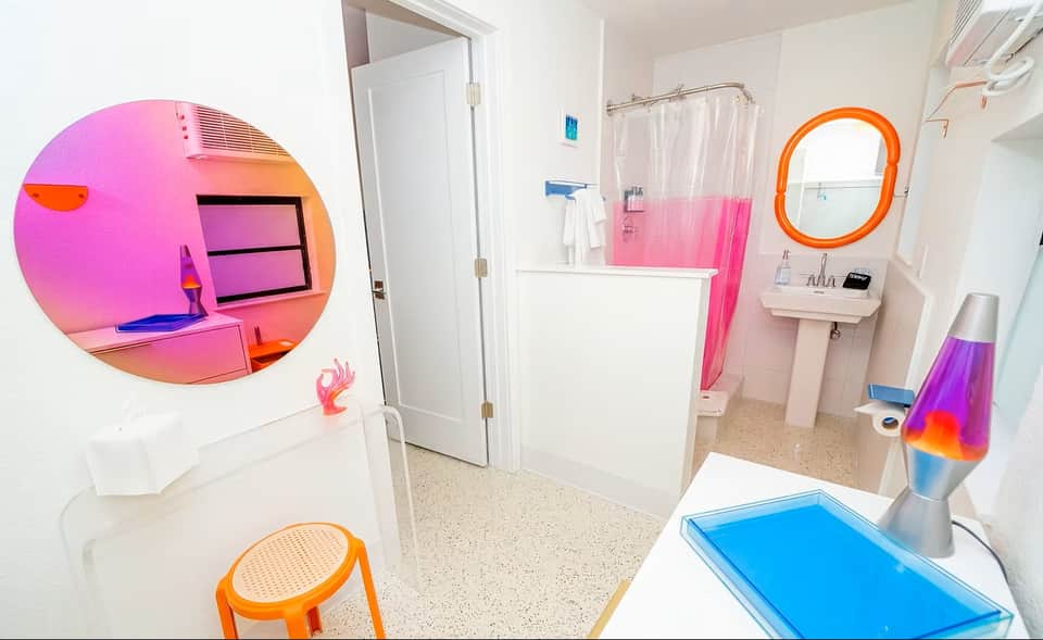 Colorful bathroom with pink shower curtain, orange circular mirror, neon pink circular wall art, and blue lava lamp decoration