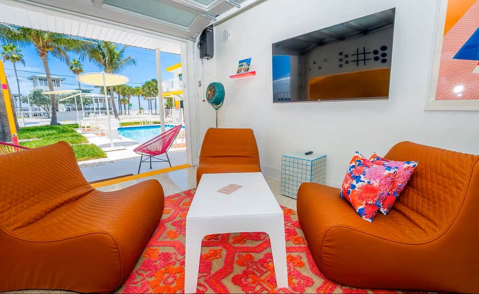 Bright indoor lounge space with orange seating, pool view through open doors, and vibrant tropical decor