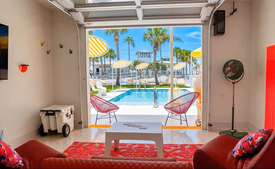 Spacious lounge opening to pool area with red modern seating, white coffee table, and palm tree views