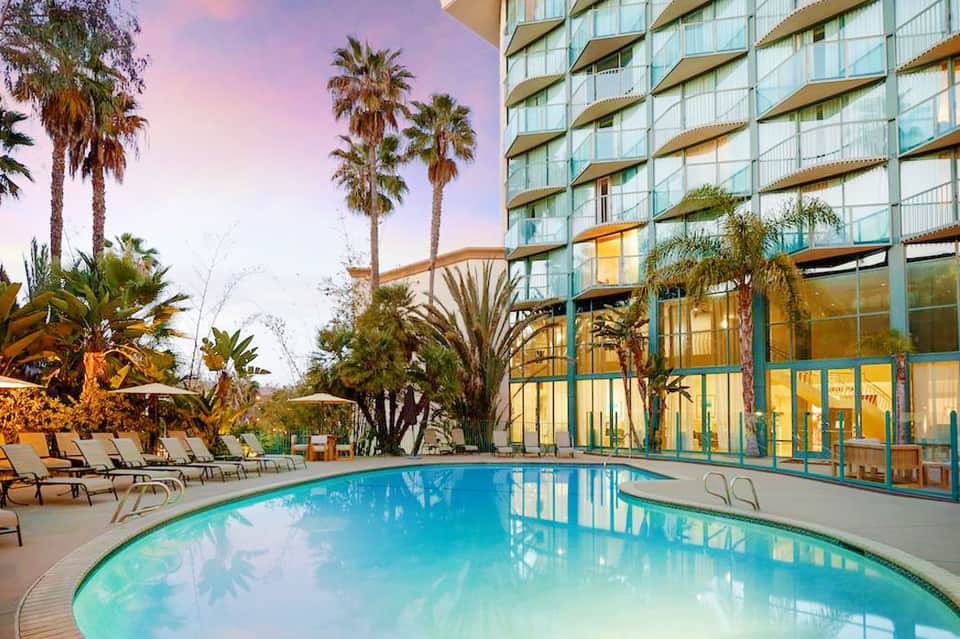 Resort pool at dusk with palm trees, lounge chairs, and modern hotel building with lit windows