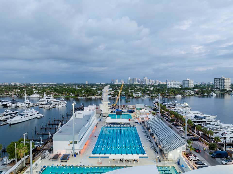 Aerial view of waterfront resort with Olympic-size lap pool, leisure pool, and surrounding marina and cityscape