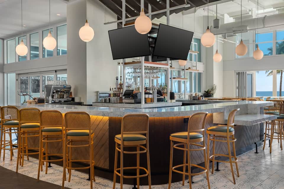 Modern hotel bar with pendant lighting, ocean views, and wood accent seating