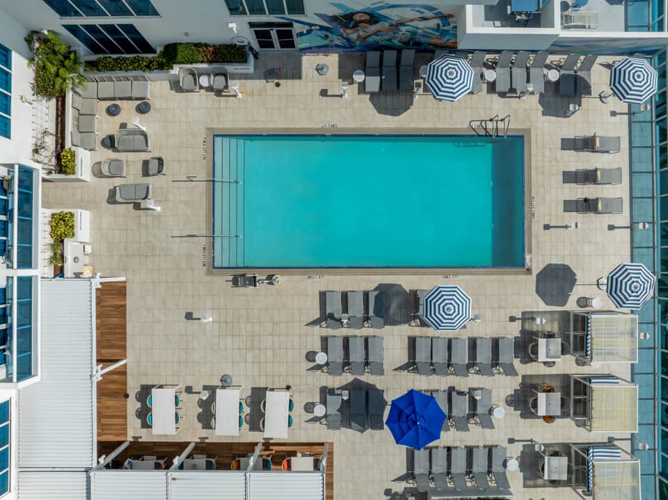 Rooftop pool deck with turquoise lap pool, striped umbrellas, and lounging areas