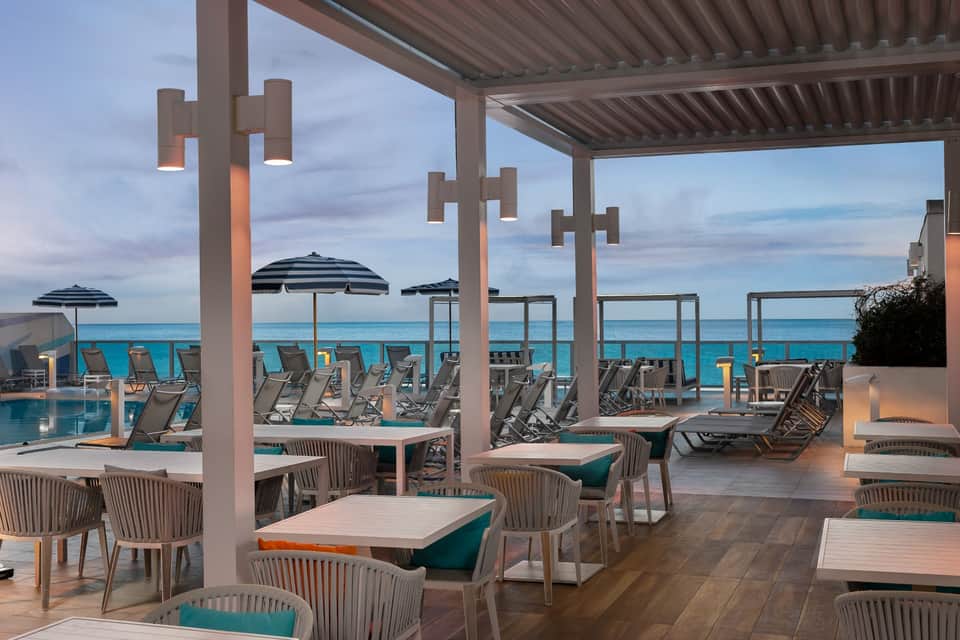 Waterfront dining terrace with striped umbrellas, lounge chairs, and turquoise ocean view