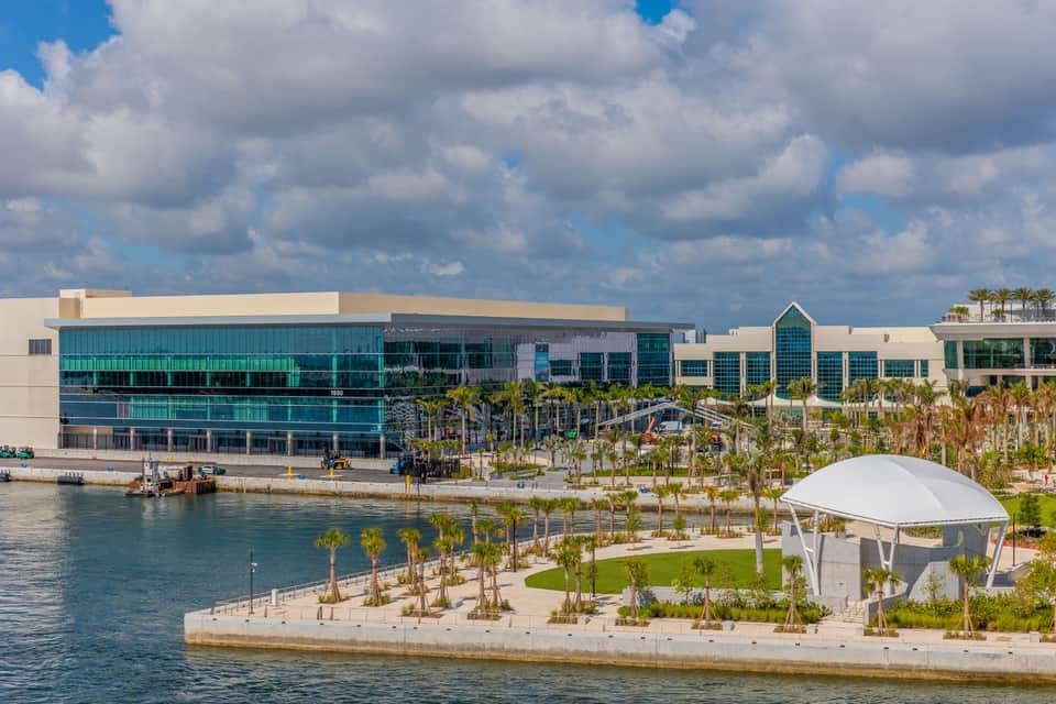 Modern waterfront facility with turquoise glass panels, palm landscaping, and white tent pavilion