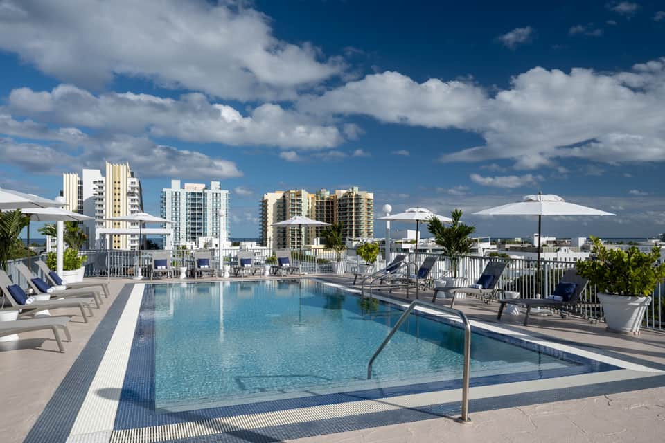 Modern rooftop pool deck with lounge chairs, white umbrellas, and high-rise hotel towers cityscape