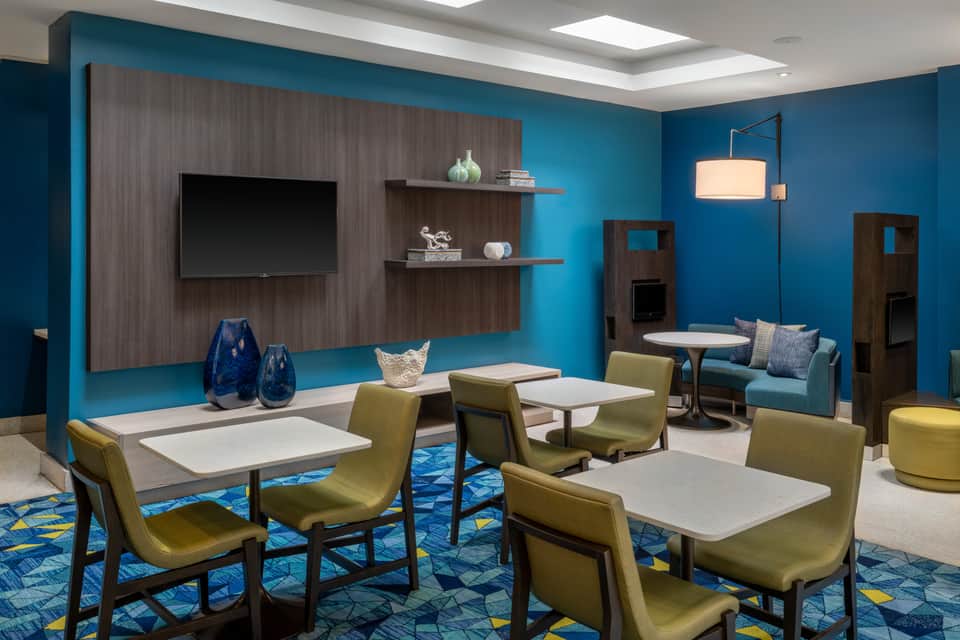 Contemporary hotel lobby with bold teal walls, dark wood accents, lime green chairs, and casual seating areas