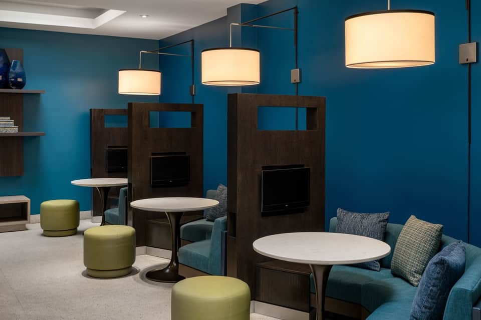 Hotel lounge with teal walls, wooden booth seating, cream pendant lights, lime poufs, and casual gathering spaces