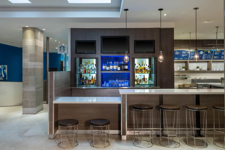 Upscale bar with dark wood shelving, blue accent lighting, multiple television screens, and elegant cocktail seating