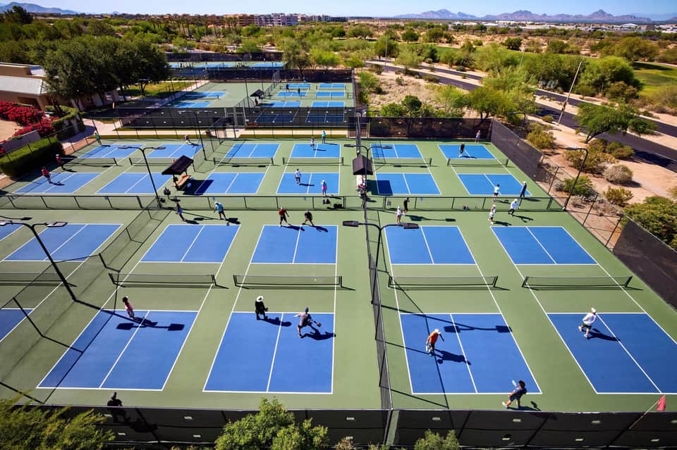 Aerial view of multiple blue and green pickleball courts in a desert resort community