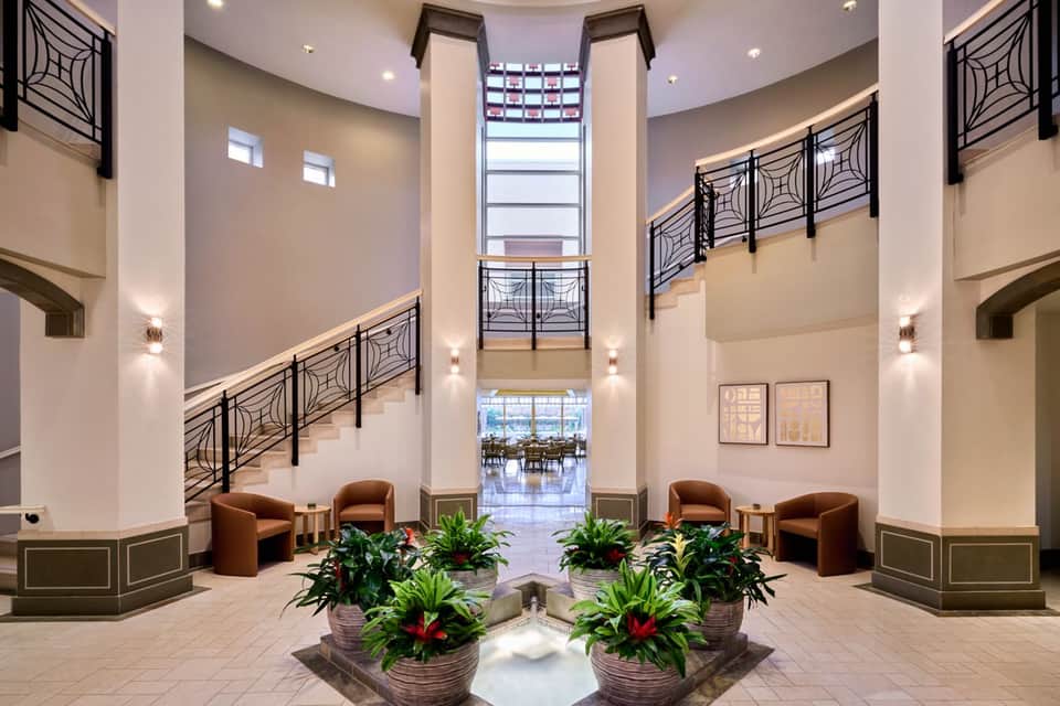 Modern multi-story hotel atrium with spiral staircase, geometric railings, and plants