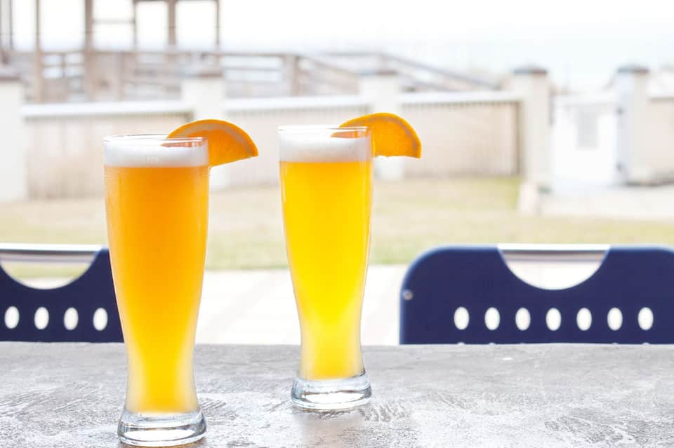 Two glasses of fresh orange juice with orange slices on a sunny poolside terrace