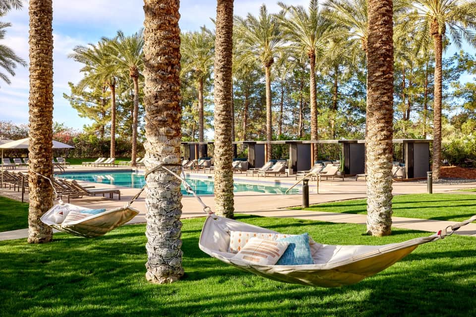 Resort poolside with hammocks between palm trees, lounge chairs, and pool cabanas