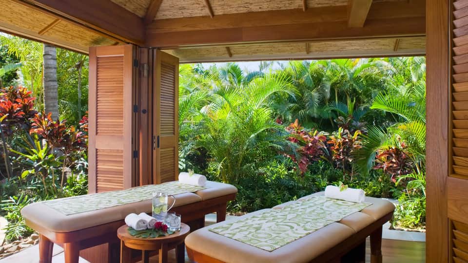 Luxury spa treatment room with massage tables overlooking tropical garden with palm trees and colorful flowers