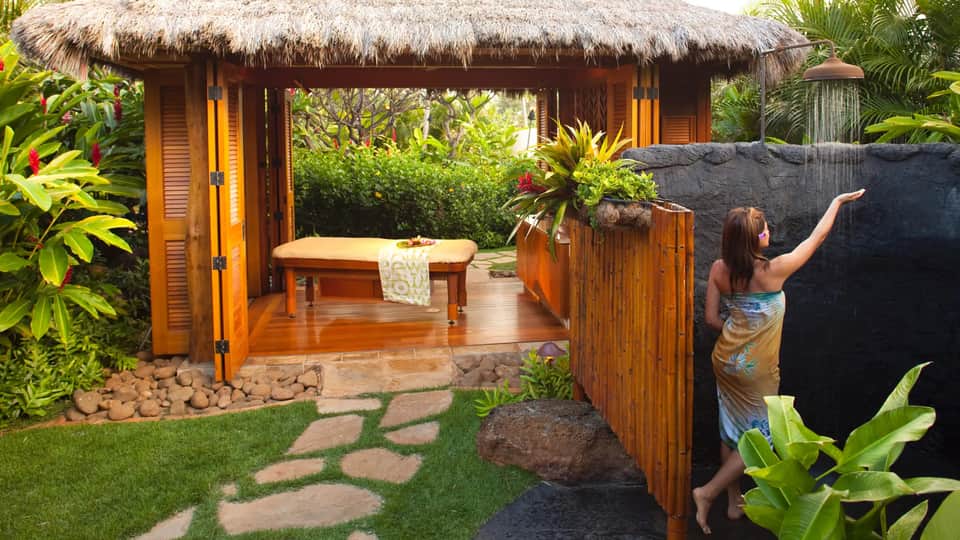 Outdoor spa pavilion with thatched roof, wooden deck, massage bench, and lush tropical vegetation