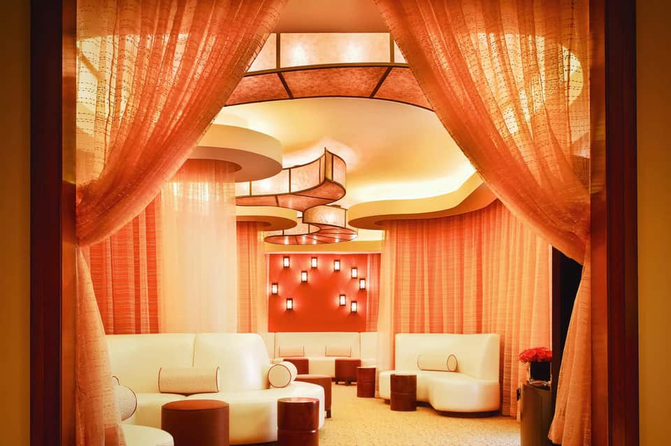 Elegant spa lounge with orange curtains, cream seating, curved ceiling details, and warm contemporary design