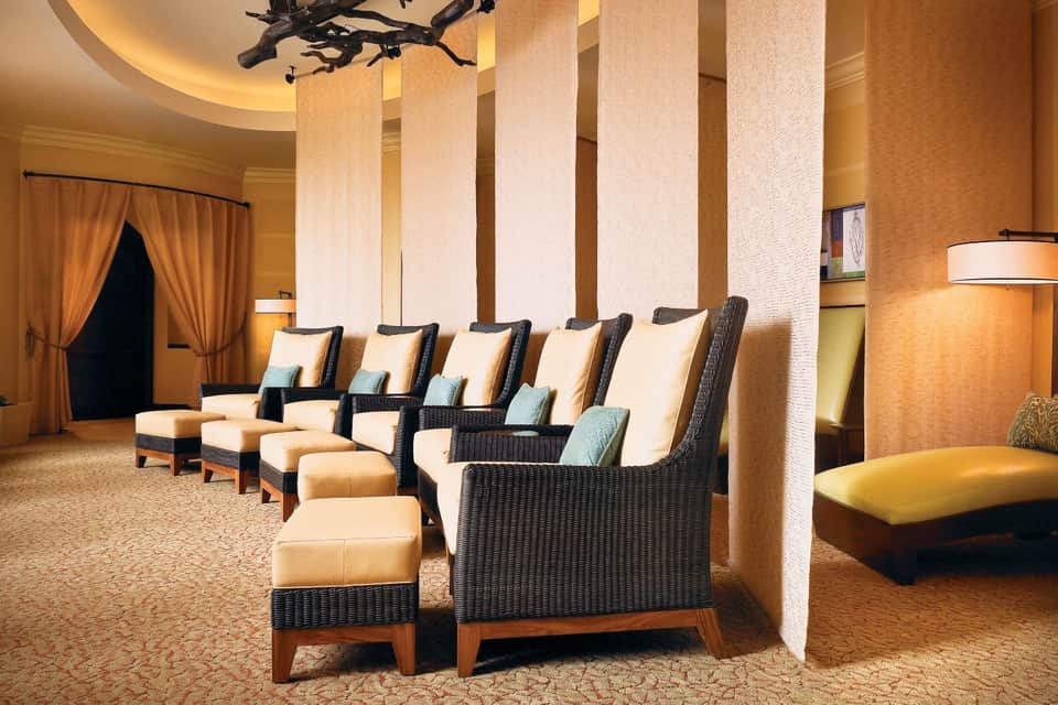 Spa relaxation room with rows of cushioned recliners, tall columns, warm lighting, and sophisticated decor