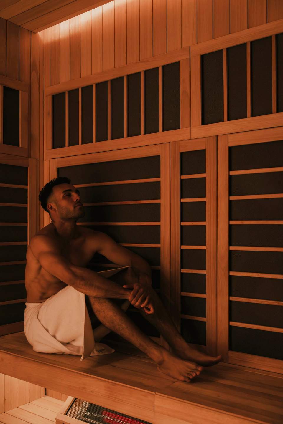 Indoor sauna with natural wood paneling, infrared heater walls, and warm amber lighting