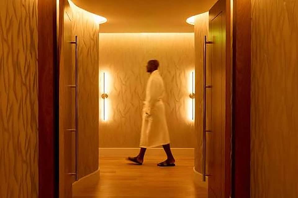 Modern hotel corridor with warm wood paneling and LED lighting, guest walking through hallway