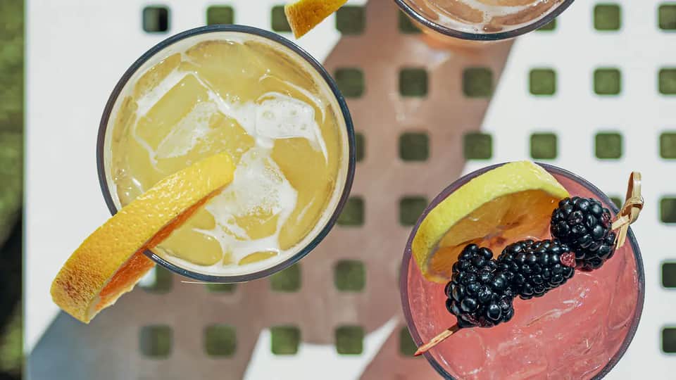Overhead view of two vibrant cocktails: yellow citrus drink and pink berry cocktail with garnish