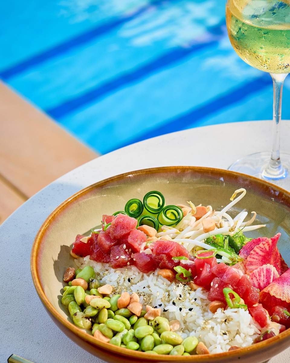 Gourmet poke bowl with sushi rice, tuna, edamame and radish by poolside with wine glass