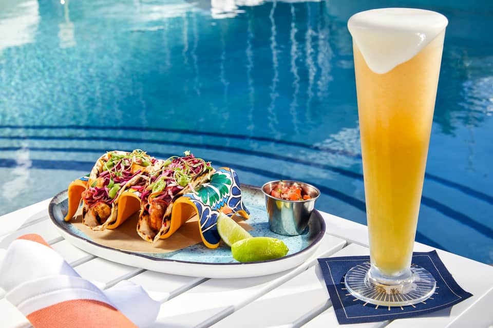 Fish tacos with fresh toppings and beer served poolside at resort with ocean backdrop