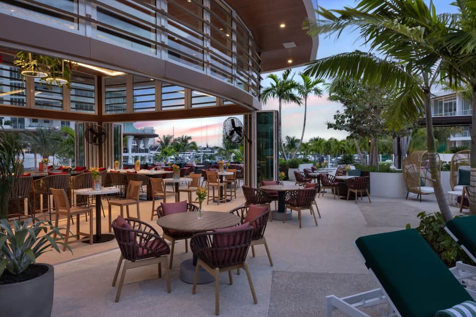 Modern beachfront restaurant terrace at sunset with palm trees, ocean views and comfortable seating