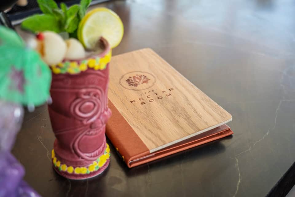 Tropical cocktail in decorative tiki glass with menu on wooden table at resort bar