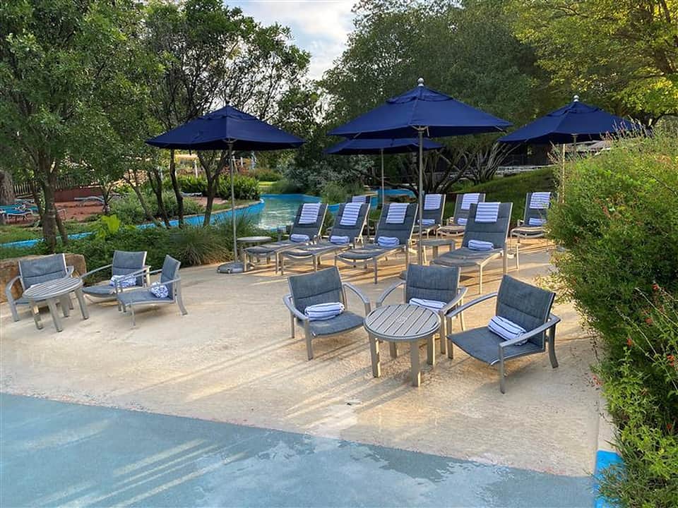 Poolside lounge area with blue umbrellas, gray cushioned chairs, and blue water feature in foreground
