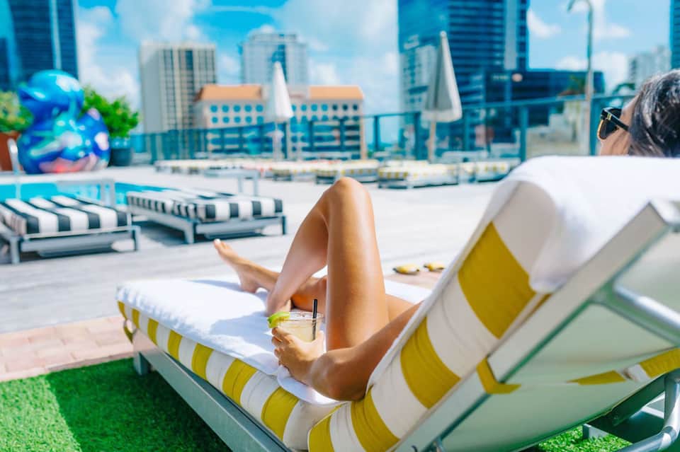 Woman relaxing on striped lounger with cityscape and rooftop pool in background