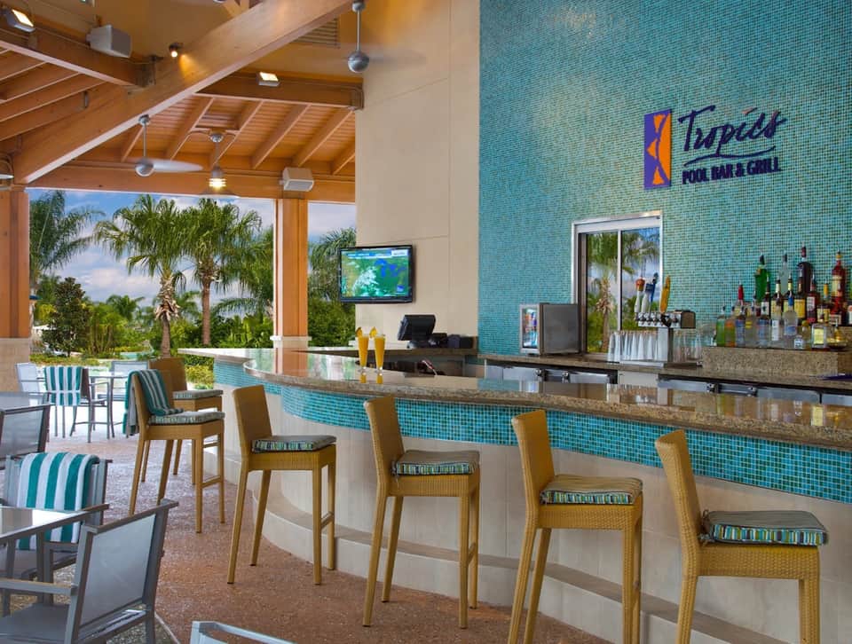 Tropical pool bar with turquoise tile, wooden beams, palm trees, and striped bar stools