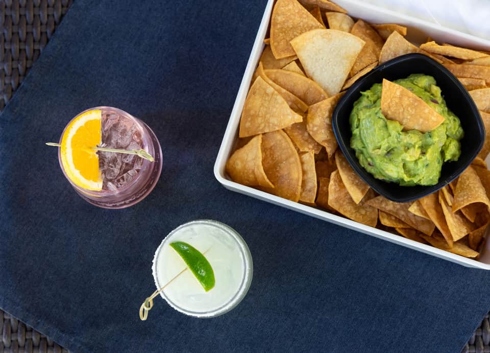 Cocktails and guacamole with tortilla chips on a dark blue outdoor table setting