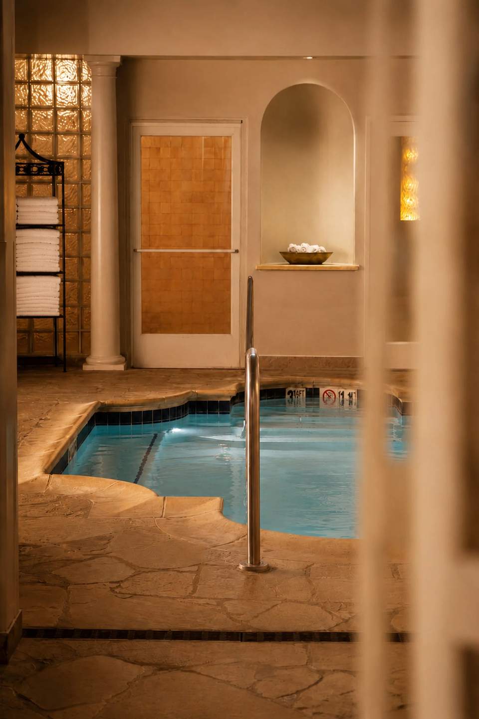 Serene spa bathroom with small soaking tub, arched alcove, warm lighting, and travertine floors