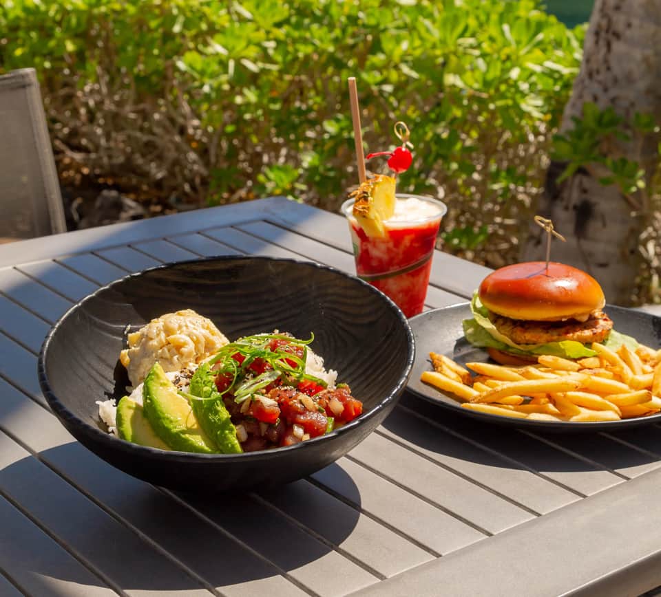 Gourmet meal with tuna poke bowl and burger served outdoors with tropical beverage