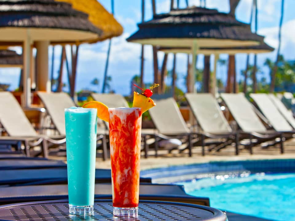 Colorful cocktails by pool with lounge chairs, umbrellas, and ocean views
