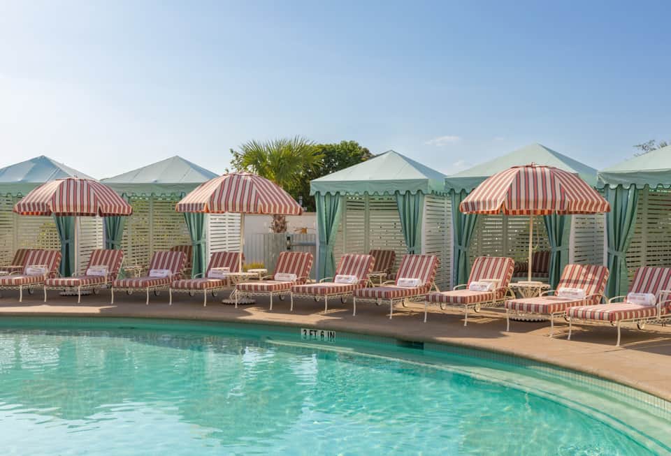 Resort pool with turquoise water surrounded by red and white striped umbrellas and mint green cabanas