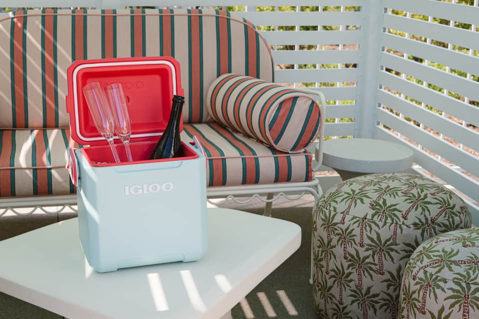 Striped beach towels, cooler with champagne glasses, and palm-patterned pillow on lounge chair