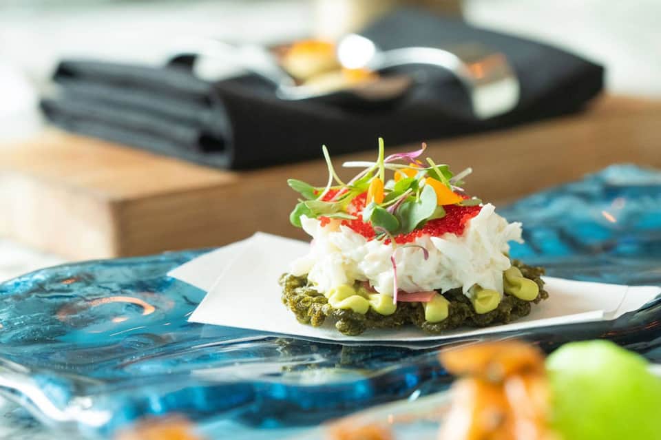 Plated appetizer with crab cake, vegetables and microgreens on white square plate