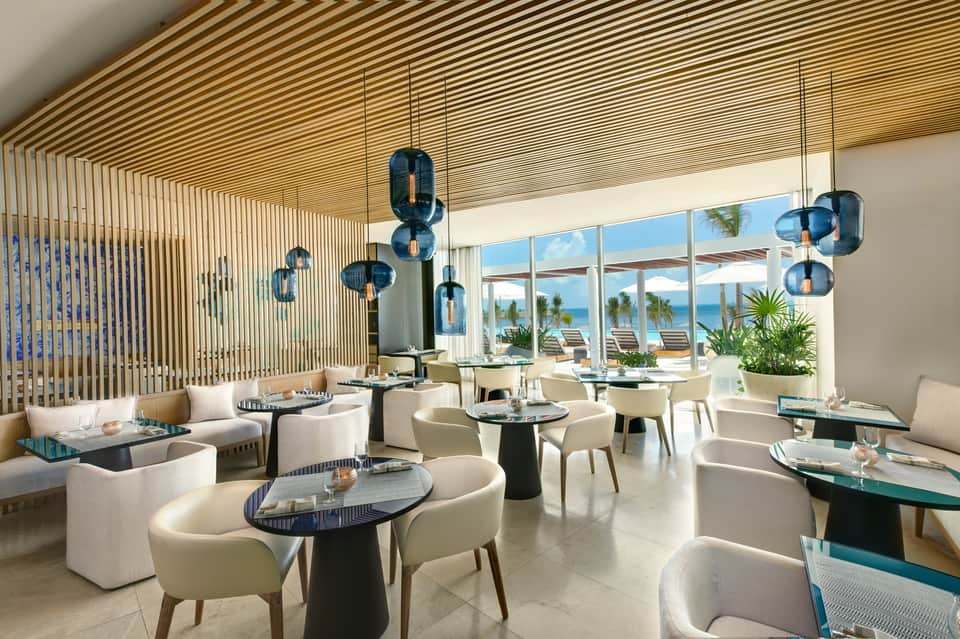Modern fine dining restaurant with blue pendant lights, white seating, ocean view, and contemporary design