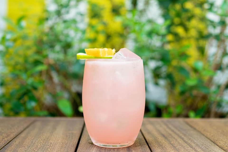 Pink cocktail with pineapple garnish against lush green garden backdrop