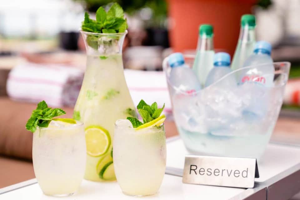 Outdoor table with refreshing lemonade cocktails garnished with mint and lemon slices, water bottles in background