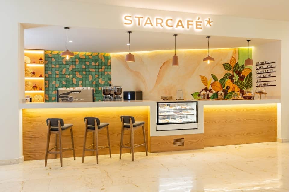 Modern Starcafé interior with green tile accent wall, pendant lighting, wooden bar seating, and sunflower artwork